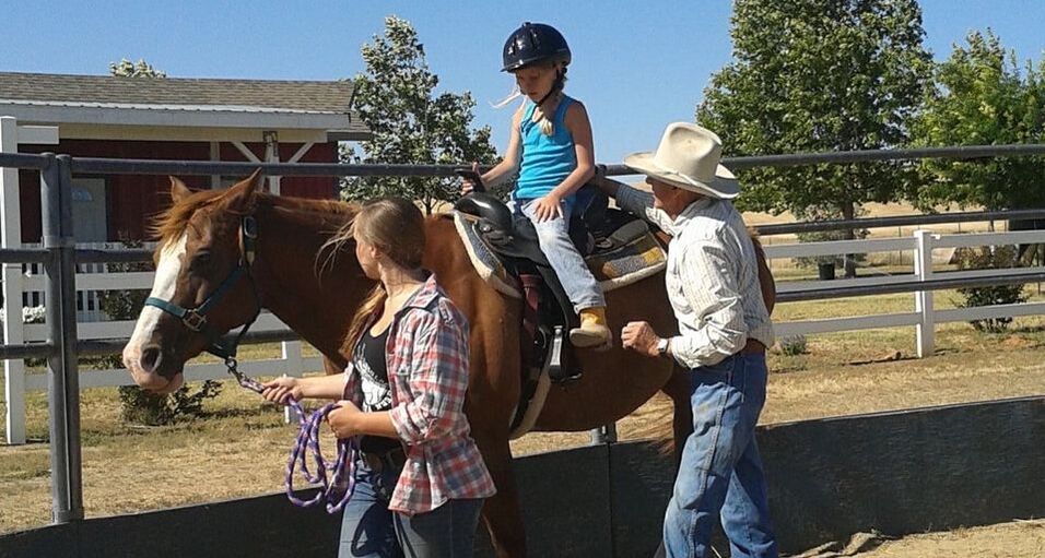 Horse wrangler volunteers help youth ride in the ring.